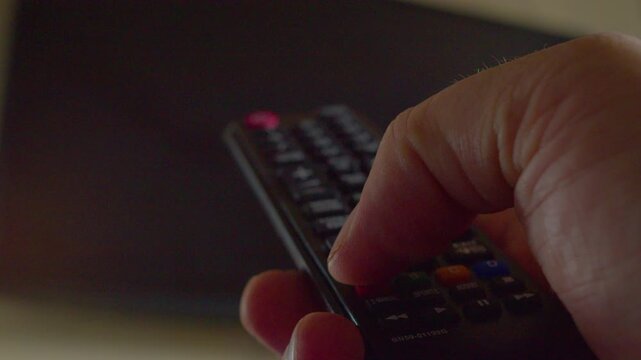 First-person view of a man's hand using a remote control to navigate a TV menu, close-up, shallow depth of field.