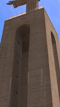 Low angle view of the Santuario de Cristo Rei sanctuary of christ the king monument with a stone cross in the foreground under a blue sky in Almada Portugal