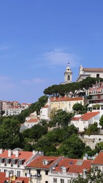 Panoramic view of Portugal Lisbon from Miradouro da Senhora do Monte or Our Lady of the Mount lookout with traditional orange tile roofs and colorful buildings under a blue sky in panorama
