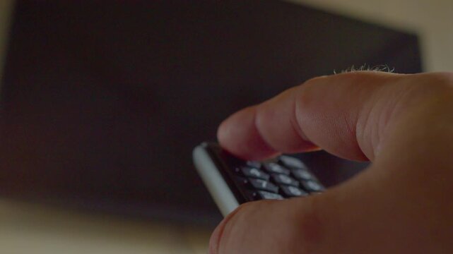 First-person view of a man's hand repeatedly pressing a remote control, unsuccessfully trying to turn on a modern wall-mounted TV. Close-up.Shallow depth of field.