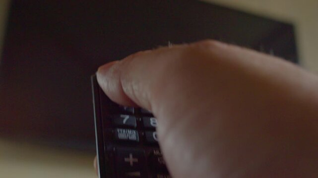 First-person view of a hand using a remote control to turn on a modern smart TV hanging on a wall, close-up, shallow depth of field.