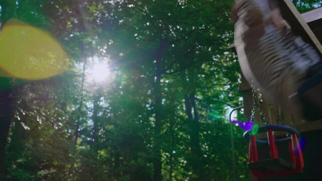 Young child swinging on backyard playset surrounded by forest trees and glowing summer sunlight capturing carefree childhood adventure outdoor freedom and family living