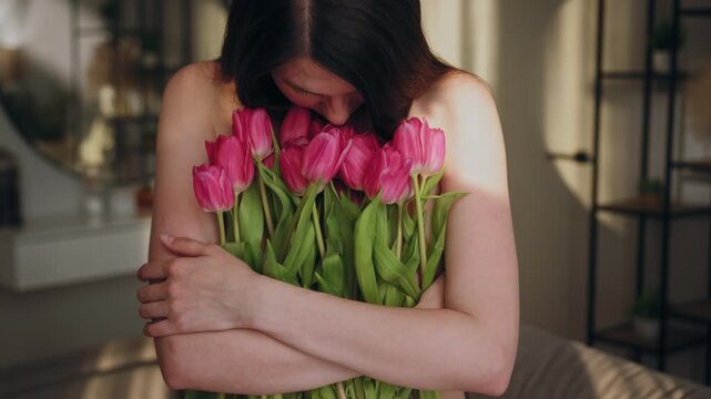 Woman embraces pink tulips, her face hidden, in soft indoor lighting. The gentle moment conveys affection, serenity and the delicate beauty of floral appreciation