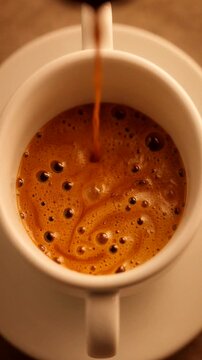 Fresh espresso being poured into a white cup, showing rich crema and bubbles in close view.