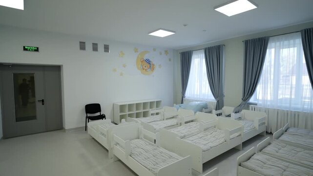 Spacious and clean dormitory features rows of neat toddler beds. Minimalist interior design with wall decorations creates calm environment