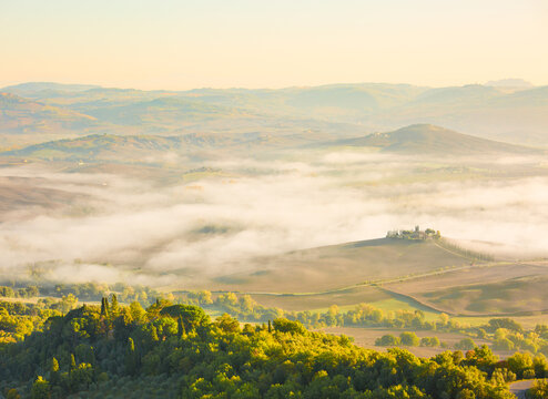Hilly fields in the foggy valley after sunrise in autumn, Tuscany, Italy.