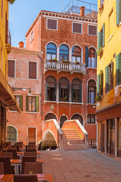 View of the small street with colorful old houses,small footbridge and street cafe in Venice on a sunny day, Italy.