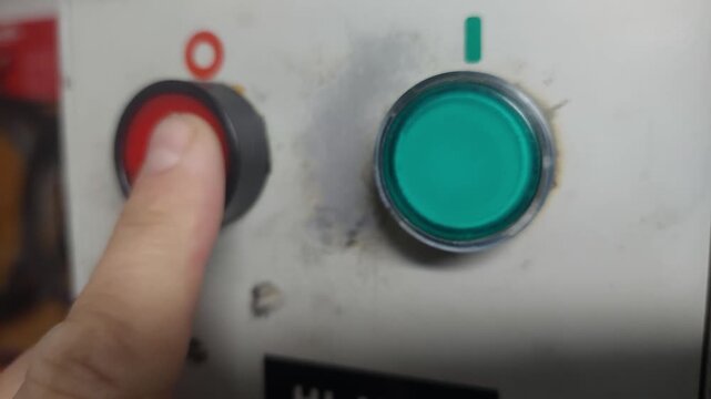 Worker pressing a green start button and then a red stop button on a machine control panel