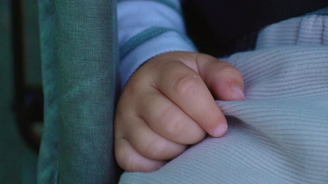 Close up of toddler hand gently gripping blanket during stroller nap capturing comfort, security and authentic peaceful childhood rest