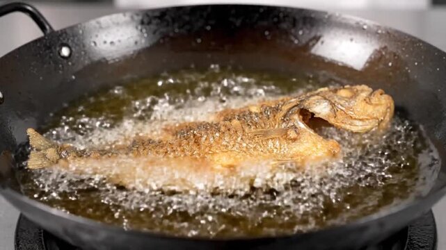 Close-up of a whole fish being deep-fried in a wok with hot oil, creating a crispy golden-brown texture, a traditional cooking method.