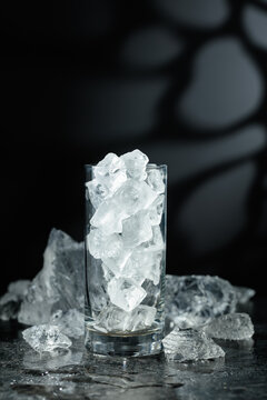 Crushed ice and a glass with ice on a black stone table.