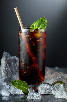 Cola with ice and mint in misted glass on a black background.