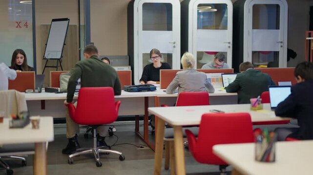 Busy professionals are focused on their tasks, working at individual desks within a collaborative office space. An active and productive atmosphere fills this modern co-working environment.