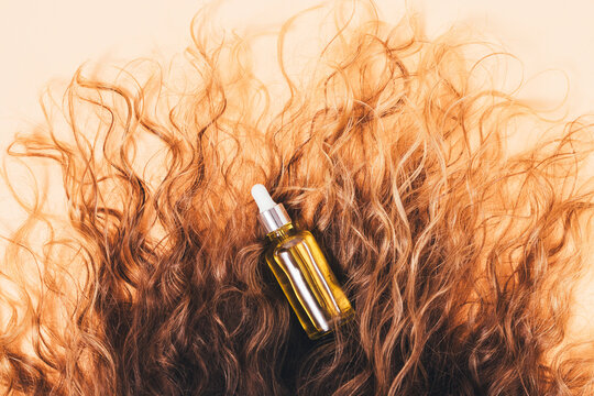 Shiny serum bottle surrounded by voluminous, wavy brown hair