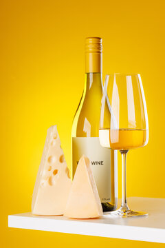 White wine with cheese pieces on yellow background gourmet composition