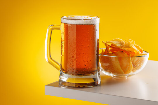 Beer mug with foam and chips on yellow background snack setup