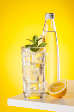 Sparkling water with lemon and bottle on yellow background refreshment