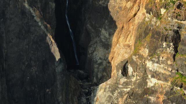 A Thin, Elegant Waterfall Cascades Down a Deep and Moody Volcanic Fissure, Surrounded by Stark Contrasts of Shadow and Golden Sunset Light on the Rugged Cliffs of Flores Island