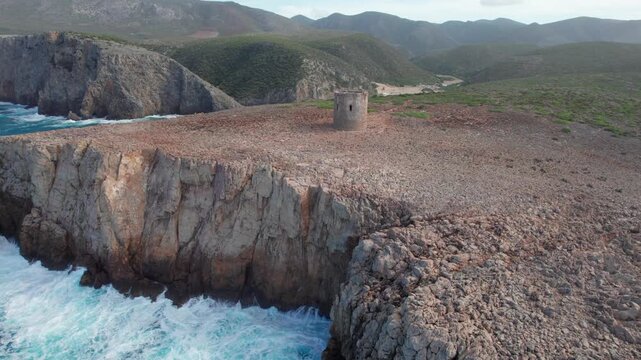 Dramatic aerial footage revealing the ancient stone watchtower of Cala Domestica, perched on a sheer cliff above the churning blue sea