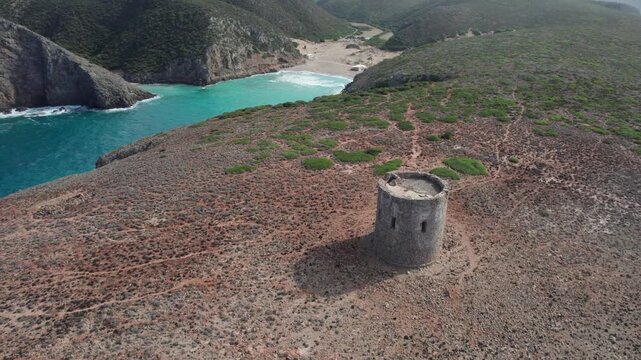 Majestic aerial view flying over the historic Torre di Cala Domestica, revealing the beautiful turquoise sea and sandy beach in Sardinia, Italy