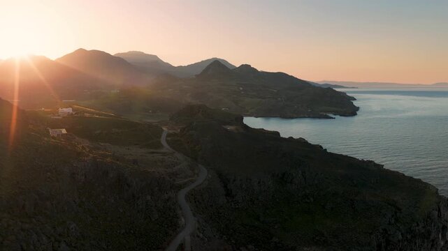 Beautiful sunrise scenery on the coastline of Island Crete with winding road through the high mountains, drone aerial view
