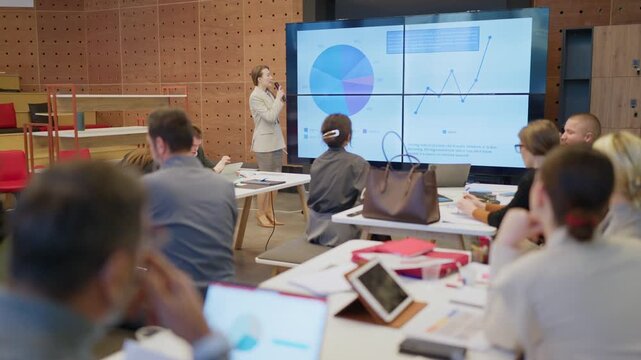 A businesswoman presents data and analytics to colleagues during a corporate meeting. Employees actively listen and learn from the presentation in a modern office setting.