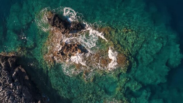 Aerial video in the Mediterranean sea, on Crete island, with waves splashing on rocks, directly above view
