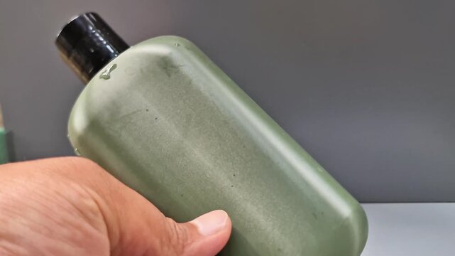 Sidoarjo, Indonesia - 20 May, 2026: Hand Holding Blank Matte Olive Green Cosmetic Bottle Mockup with Water Drops, Men's Skincare or Perfume Packaging Concept
