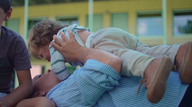 Mother lying on grass while lifting toddler during outdoor family play capturing affection, bonding and authentic carefree parenting interaction in park