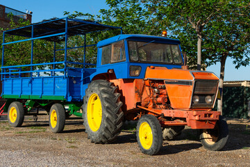 Obraz premium Old blue and orange tractor with trailer in rural field