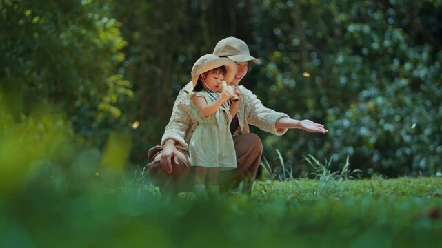 Loving Asian mother and cute little daughter watching butterflies with binoculars in green forest park, happy family exploring nature together on summer holiday, outdoor learning, adventure and parent