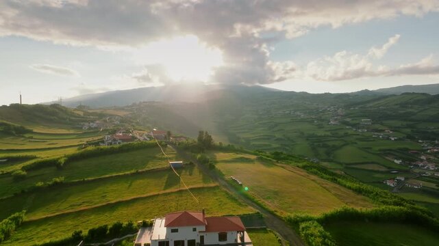Aerial view of a secluded white villa nestled in the lush, sun-drenched rolling hills of Faial Island, Azores, bathed in the soft, atmospheric glow of the golden hour.