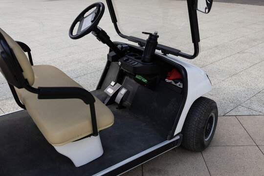 White electric golf cart parked on a modern outdoor pedestrian plaza near the seaside