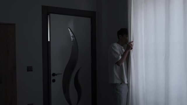 Paranoia and persecution mania concept with anxious man secretly looking through curtain, psychological fear, surveillance suspicion and unsafe home atmosphere