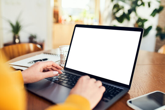 Woman typing on laptop with blank white screen at home desk