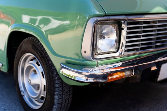 Vintage green car front view showing headlight, chrome bumper, and wheel on display