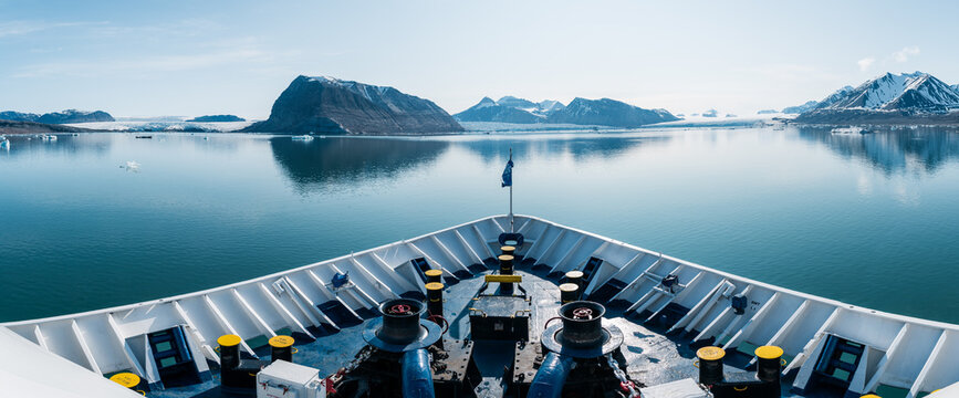 Svalbard and Jan Mayen - 27 June 2025: View of an expedition ship bow sailing through calm waters towards snow-capped mountains and glaciers under a clear blue sky.