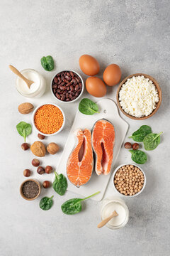 High protein food set with fresh salmon, eggs, cottage cheese, yogurt, lentils, chickpeas, beans and nuts arranged on white background with copy space