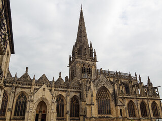 Fototapeta premium Iglesia Notre-Dame de Carentan, impresionante arquitectura romática y gótica en la Normandía francesa, con un campanario en punta y arcos en la fachada, viajando en verano de 2022