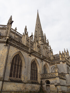 Vista lateral de la Iglesia Notre-Dame de Carentan de estilo rom&aacute;nico g&oacute;tico en la Normand&iacute;a Francesa, con c&uacute;pula puntiaguda, arcos ojivales y decoraciones en fachada, viajando en verano 2022