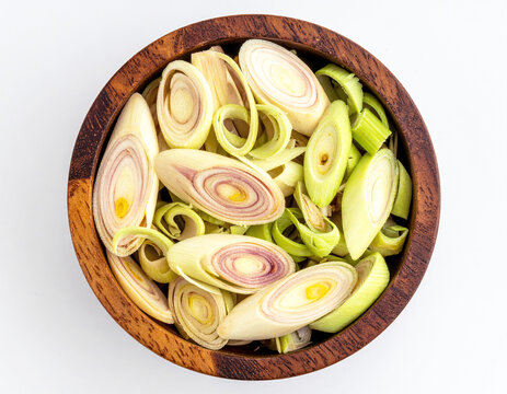 Portion of cut lemongrass in a wooden pot, seen from above, on a white background.