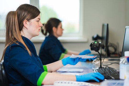 Two Technicians Collaborating Over Microscope, Shared Bench Work And Slide Inspection, Mentor In Background