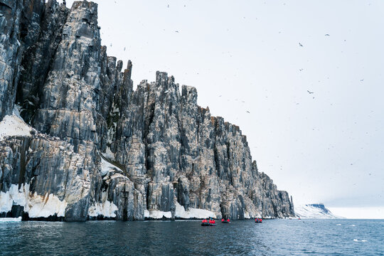 View of Alkefjellet basalt cliffs with nesting seabirds and tourists in small red boats on the water Svalbard, Svalbard and Jan Mayen.