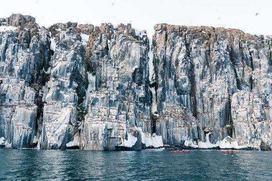 View of the towering basalt cliffs of Alkefjellet with nesting birds and people in red kayaks on the water in Svalbard, Svalbard and Jan Mayen.