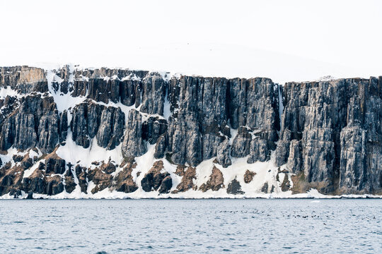View of Alkefjellet bird cliffs featuring towering basalt columns and snow patches above the cold sea Svalbard, Svalbard and Jan Mayen.