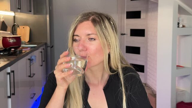 Woman Drinks Water. Blonde Woman Pauses To Drink Water In Peaceful Kitchen Setting During Her Meal
