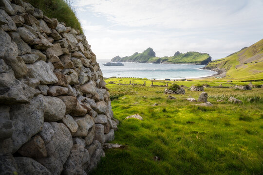 View of the historic stone walls and green hills of Hirta island overlooking a bay with a cruise ship Scotland, United Kingdom.