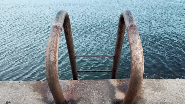 Video in medium shot, static high angle; showing a concrete edge with staircase railings overlooking a calm sea in the waters of rio de la plata estuary, montevideo city, uruguay