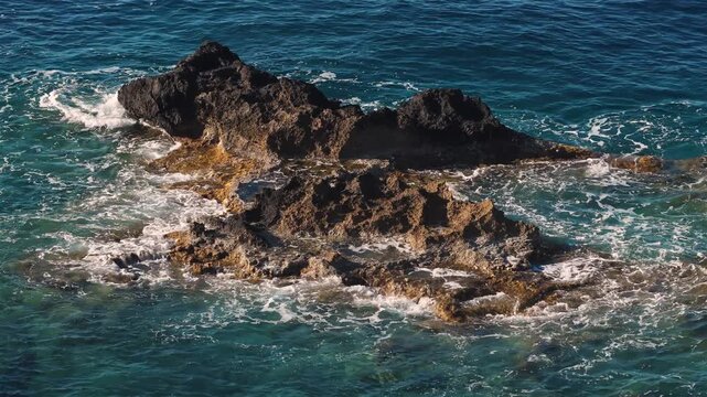 Drone video in the Mediterranean sea, on Crete island, with waves splashing on rocks, above view
