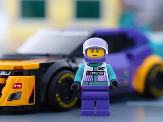 Obraz premium Tambov, Russian Federation - January 02, 2026 Lego NASCAR Next Gen Chevrolet Camaro ZL1 driver minifigure standing near his car in a city street.